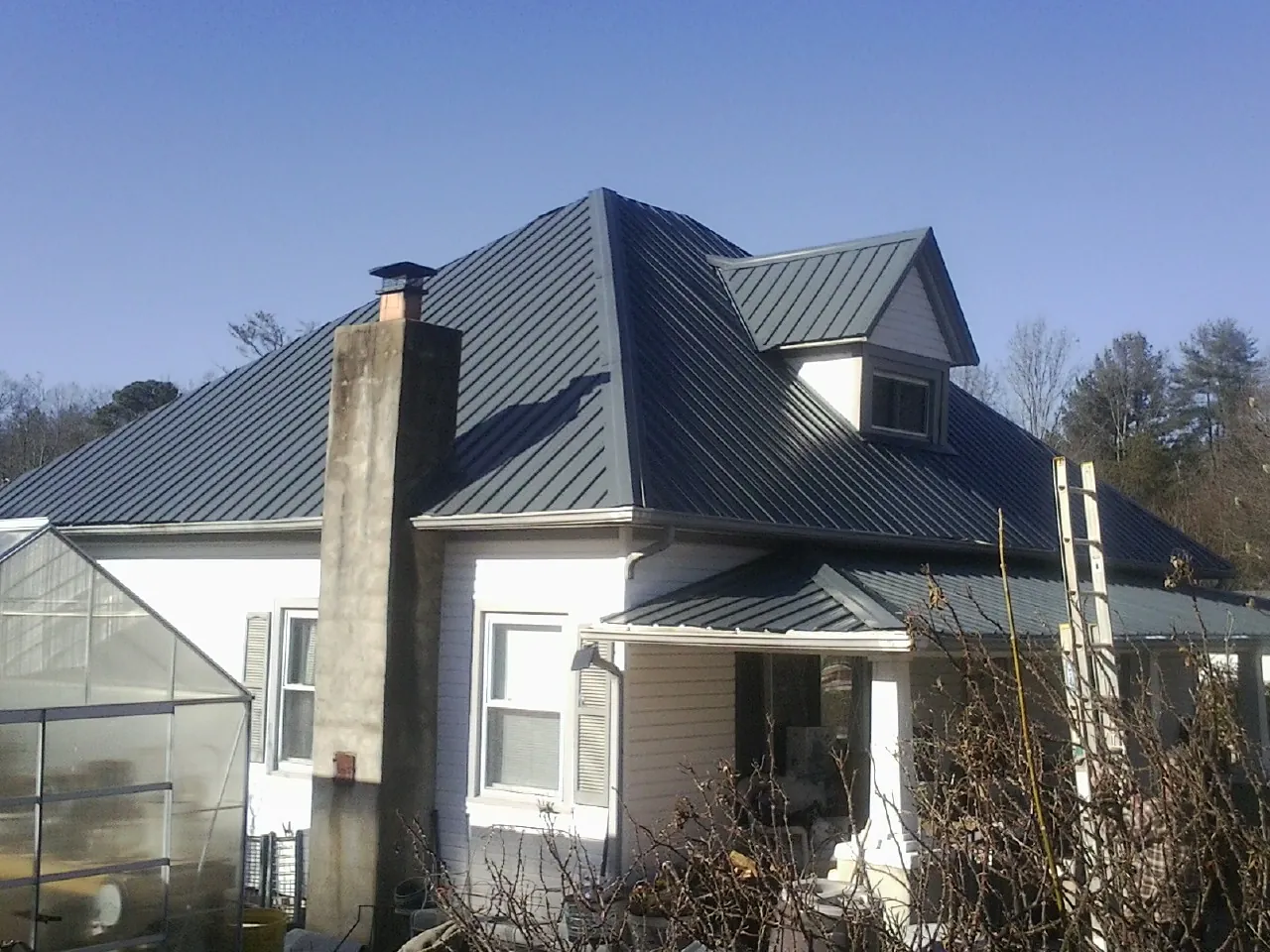 Dark blue standing seam metal roof on a white farmhouse with dormer — Slate & Tile Roof Repair by Roofing Brothers in Wilsons