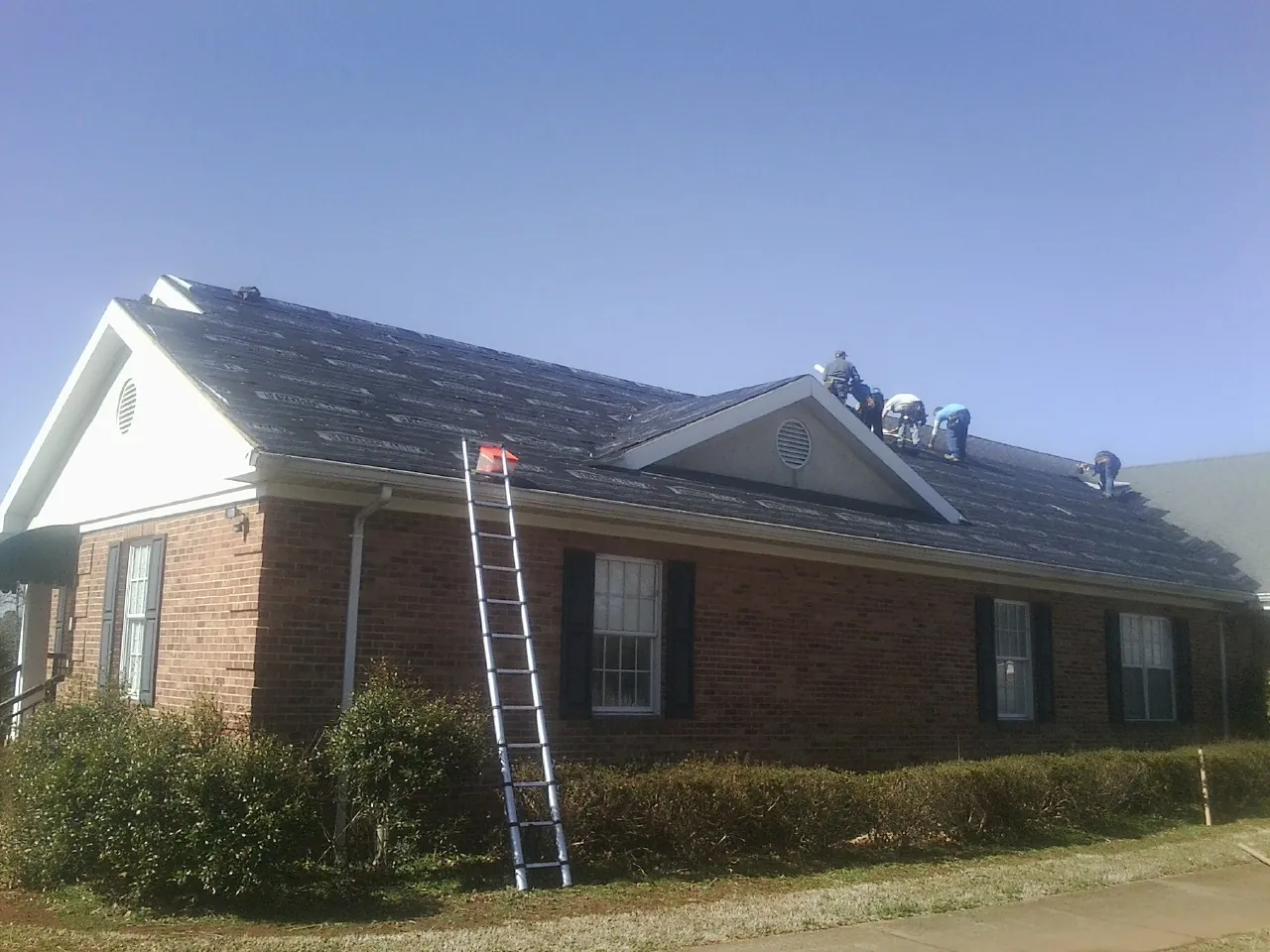 Crew tearing shingles off a brick ranch roof with a ladder set — Emergency Roof Repair work by our crew in Wilsons