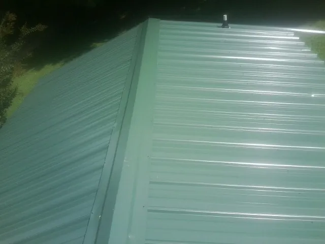 New green metal panels meeting at the ridge of a roof — Flat Roof Repair work by our crew in Wilsons