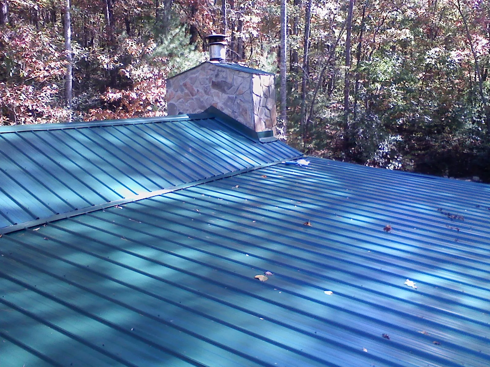 New green metal roof and stone chimney surrounded by autumn woods in Wilsons