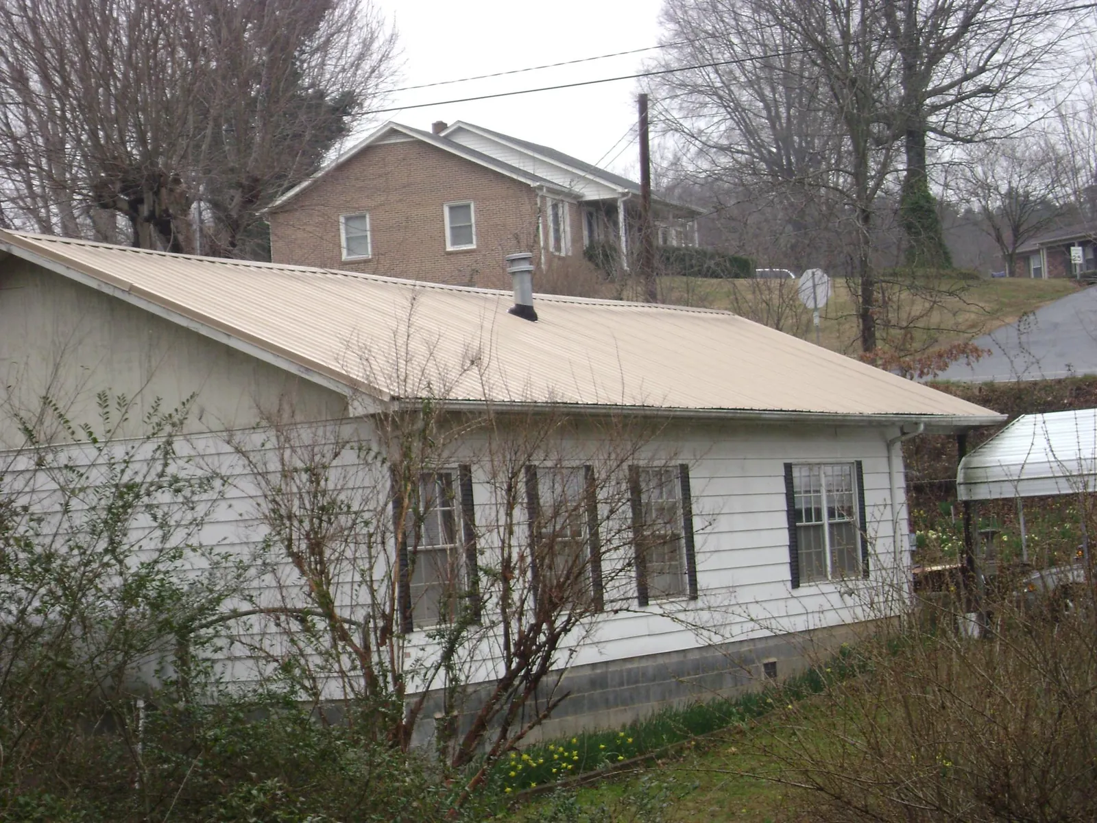 Tan metal roof on a white sided house set into a hillside — Commercial Roofing by Roofing Brothers in Wilsons