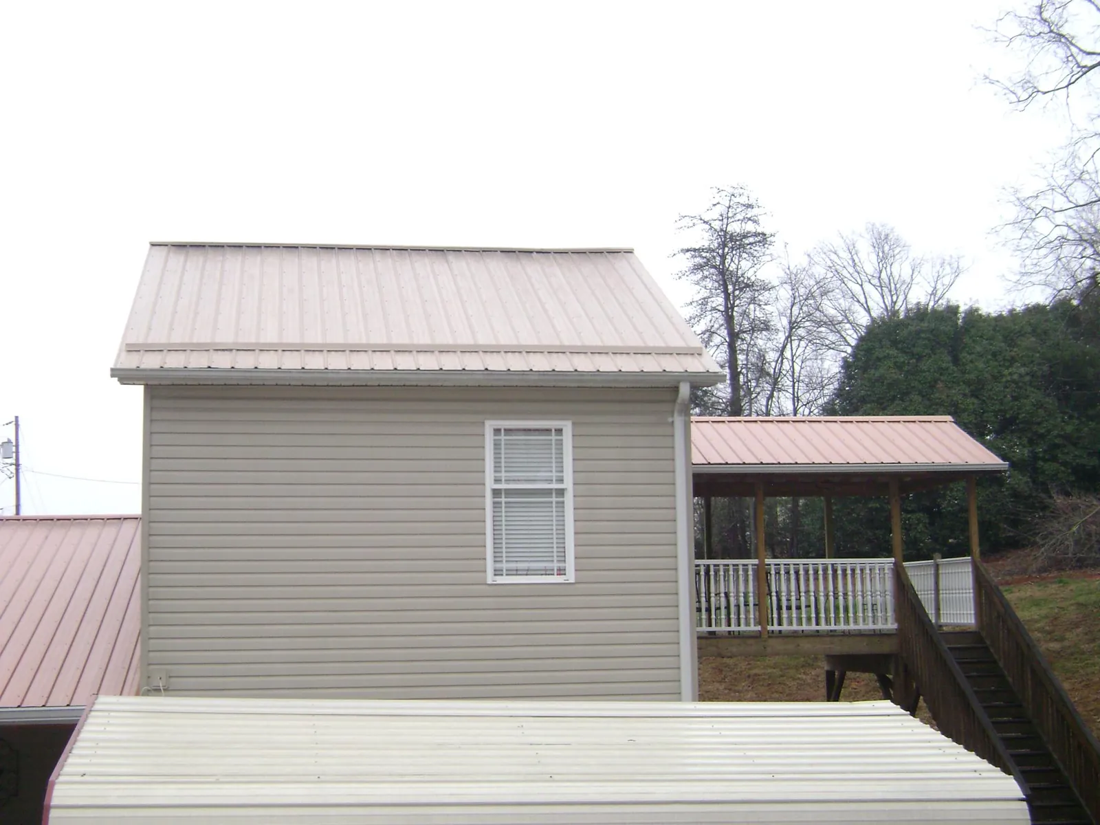 Tan metal roofs on a two story addition and attached porch, from a Roof Replacement job in Wilsons